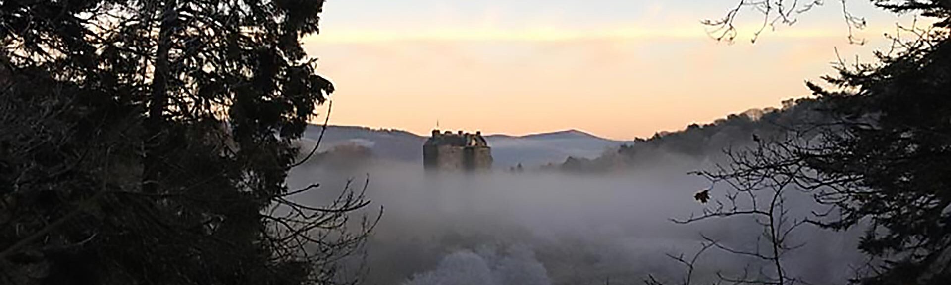 Mist-covered Neidpath Castle in Scotland viewed from the nearby forest on a crisp winter morning.